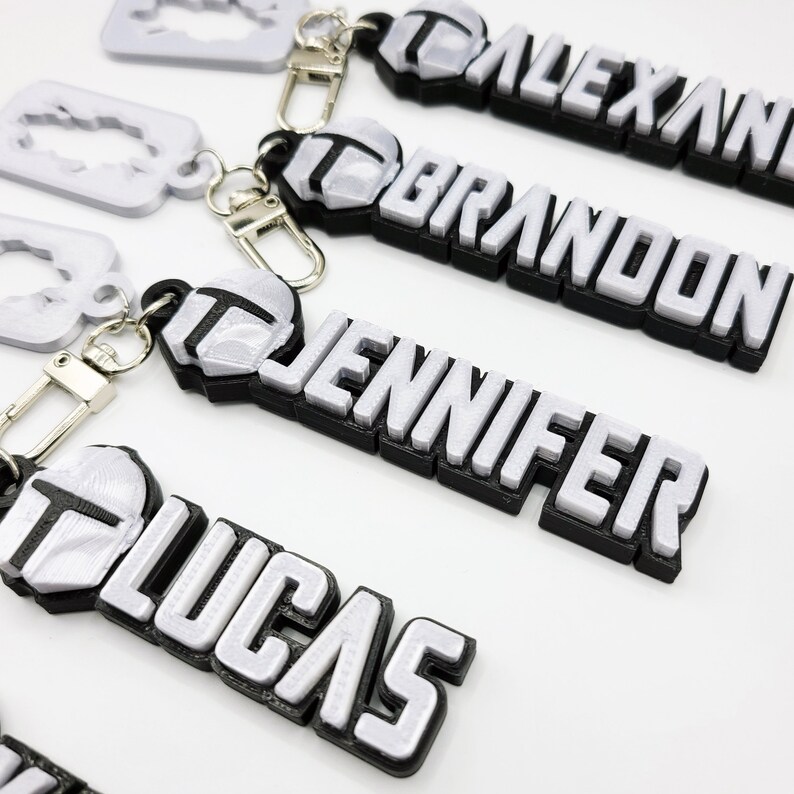 May include: Four silver keychains with black trim, each featuring a different name:  "ALEXANDRIA", "BRANDON", "JENNIFER", and "LUCAS".
