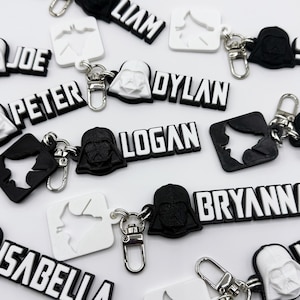 May include: A collection of personalized keychains featuring black and white 3D printed Darth Vader heads and names, including Joe, Peter, Liam, Dylan, Logan, Bryanna, Isabella.