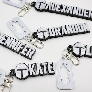May include: Five personalized keychains with a silver Mandalorian helmet design and black lettering. The names on the keychains are Jennifer, Brandon, Alexander, Kate, and a blank keychain with a Mandalorian silhouette.