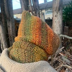 May include: A handmade crochet hat and cowl set. The hat is a pointed style, with a gradient of green, orange, and brown. The cowl is a matching colour and texture. The set is made of a thick, textured yarn.