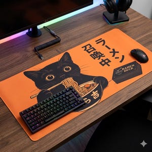 Pode incluir: Um tapete de secretária retangular laranja com a ilustração de um gato preto a comer ramen com pauzinhos. O tapete inclui texto em japonês e um gráfico de uma caixa com a etiqueta RAMEN DECK. Um teclado mecânico e um rato pretos estão em cima.