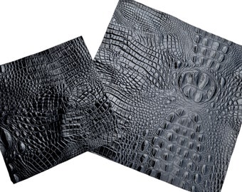 May include: Two pieces of black faux crocodile leather. The leather has a detailed, textured pattern with scales and ridges, mimicking the look of crocodile skin. The pieces are angled against a white background.