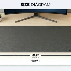 May include: A rectangular dark gray desk mat with rounded corners. The size diagram indicates a depth of 12.2 inches and a width of 31.5 inches. The mat features a textured surface and a small logo in the bottom right corner.