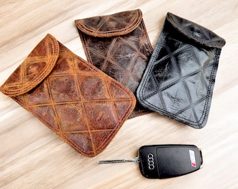 May include: Three leather phone cases in brown, black, and dark brown with a quilted pattern. The cases have a flap closure. A black car key with the Audi logo is in the foreground.