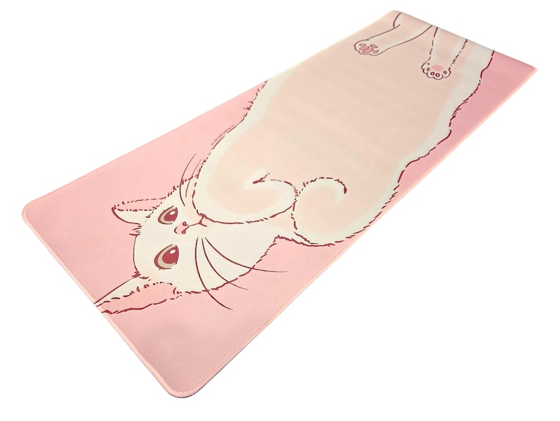 May include: A rectangular yoga mat featuring a light pink background with a large, cream-colored cat illustration stretched across the surface. The cat has dark pink outlines, large eyes, and visible paw pads, extending from the bottom left to the top right.