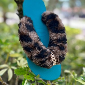 May include: Teal blue flip-flop with a brown and black faux fur strap and a gold rhinestone embellishment.