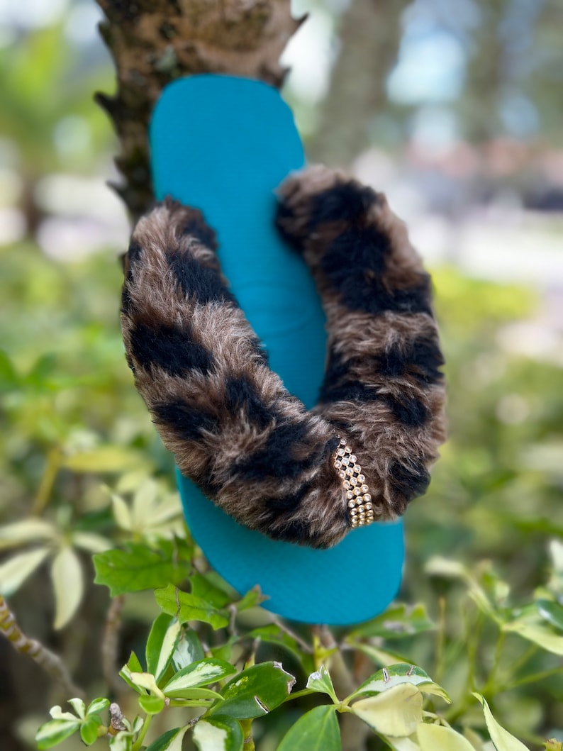 May include: Teal blue flip-flop with a brown and black faux fur strap and a gold rhinestone embellishment.