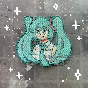 May include: Embroidered patch depicting a teal anime character with long pigtails, a white vest, and a red tie. The patch has detailed stitching and the text "only available on marcocapone.ca and etsy".