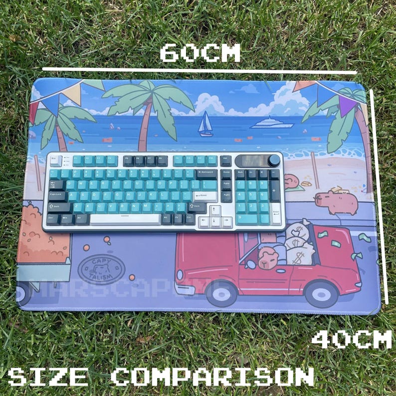 May include: A rectangular mousepad with a beach scene design, measuring 60cm long and 40cm wide. A teal and white keyboard sits on the pad. The pad features a red car with money bags and the text "CAPITALISM".