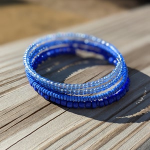 May include: A set of four blue beaded bracelets, stacked on top of each other, with the lightest blue on top and the darkest blue on the bottom.