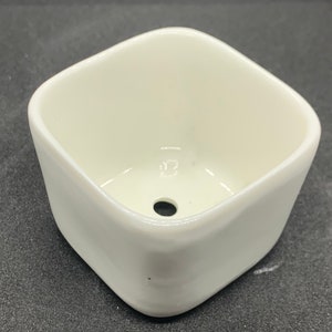 May include: A white ceramic square planter with a drainage hole in the bottom.