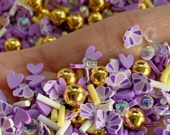 May include: Purple and gold sprinkles for baking and decorating. The sprinkles include hearts, flowers, and small gold balls.