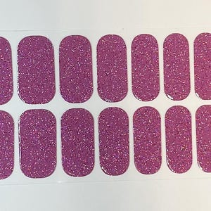 May include: A sheet of 16 pink glitter nail polish strips. The strips are arranged in two rows of eight. The strips are designed to be applied to fingernails.