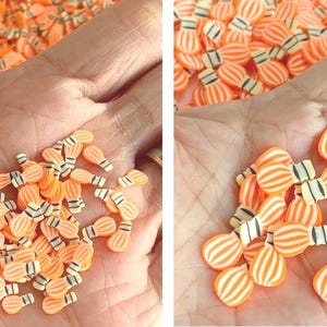 May include: Orange and white striped light bulb shaped polymer clay beads. The beads have a black and white base and are held in a hand. These beads are ideal for crafting and jewelry making.