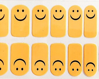 May include: A sheet of 10 yellow nail decals with black smiley face designs. Some of the smiley faces are upside down.