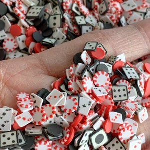 May include: A collection of red, white, and black casino-themed sprinkles. The sprinkles are shaped like dice, poker chips, and playing cards.