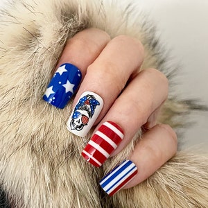 May include: Red, white, and blue nail art designs. One nail features a skull wearing sunglasses and a bandana. Other nails feature red and white stripes and blue and white stripes.