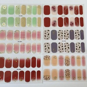 May include: Ten sheets of nail polish wraps with various designs. The designs include floral, geometric, and animal print patterns. The wraps are in shades of red, pink, beige, and brown.