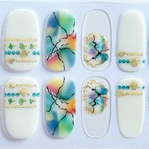 May include: A set of nail wraps featuring a variety of designs. Some nails have a white base with gold and teal accents. Others have colorful abstract designs in blue, green, and orange. The wraps are oval-shaped.