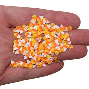 May include: A handful of candy corn-shaped sprinkles in white, yellow, and orange. These small, decorative pieces are designed for baking and crafting, perfect for adding a festive touch to Halloween treats and projects.