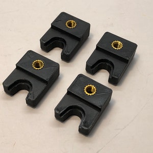 May include: Four black plastic clamps with a gold screw in the center of each. The clamps have a U-shaped opening.