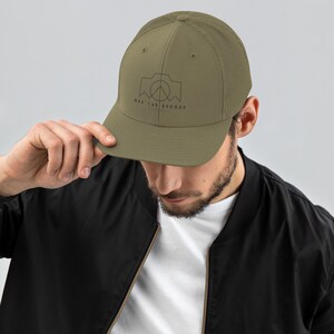 May include: A green and black mesh trucker hat with a black and white graphic of a camera with a peace sign inside and the text "Off the Record" underneath.