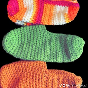 May include: Three crochet footies in vibrant colors. The top footie is striped with pink, orange, white, and yellow. The middle footie is solid green, and the bottom footie is solid orange. The text "Crochet footies" is at the top.