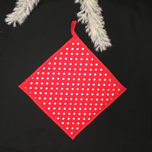 Könnte beinhalten: Roter, gesteppter Topflappen mit weißen Punkten. Der Topflappen ist rautenförmig mit einer Schlaufe zum Aufhängen.