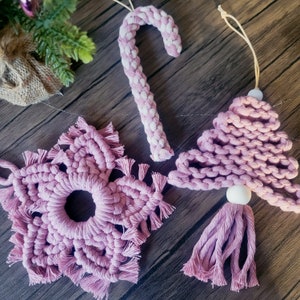 May include: Three pink crocheted Christmas ornaments: a candy cane, a star, and a Christmas tree. The ornaments are made with thick yarn and have a rustic, handmade look.
