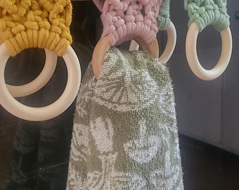 May include: Three crocheted towel rings in yellow, pink, and green hanging on a silver stove. A green towel is hanging from the pink ring.