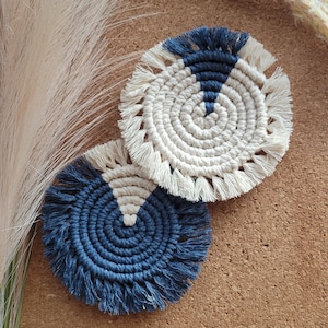 May include: Two round crocheted coasters with a fringe border. One coaster is white with a blue center and the other is blue with a white center.