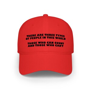 May include: A bright red baseball cap with the text "THERE ARE THREE TYPES OF PEOPLE IN THIS WORLD, THOSE WHO CAN COUNT AND THOSE WHO CAN'T" in black lettering. The cap has a curved brim and a rounded crown.