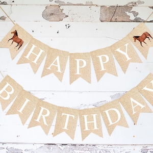 May include: A burlap banner with the words "Happy Birthday" in white letters. The banner is decorated with two brown horses on each end.