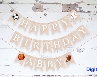 May include: A burlap banner with the words "HAPPY BIRTHDAY ABBY" in white capital letters. The banner is decorated with sports balls: a soccer ball, a baseball, a basketball, and a football. The word "Digital" is in the bottom right corner.