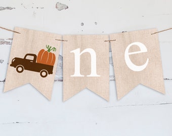 May include: A burlap banner with the word "one" in white letters. The first letter is replaced with a brown truck carrying an orange pumpkin.