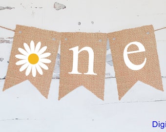 Op de afbeelding: Een banner van jute met witte letters die "one" spellen en een witte madeliefje met een gele kern. De banner is vastgemaakt met touw.