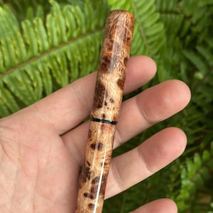 Puede incluir: Un bol&iacute;grafo de madera artesanal con un patr&oacute;n de veta de madera de burl &uacute;nico. El bol&iacute;grafo presenta un acabado pulido, mostrando los colores naturales de la madera, con tonos marr&oacute;n oscuro y marr&oacute;n claro. Una banda negra acent&uacute;a el dise&ntilde;o del bol&iacute;grafo.