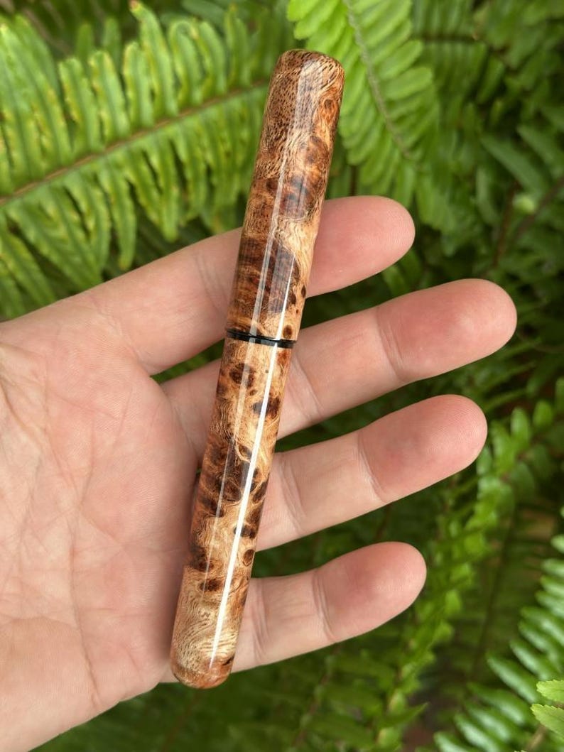 Puede incluir: Un bol&iacute;grafo de madera hecho a mano con un patr&oacute;n de veta de madera natural. El bol&iacute;grafo presenta un acabado pulido con diferentes tonos de marr&oacute;n y beige. Una banda negra acent&uacute;a el centro del bol&iacute;grafo, a&ntilde;adiendo un toque de contraste.