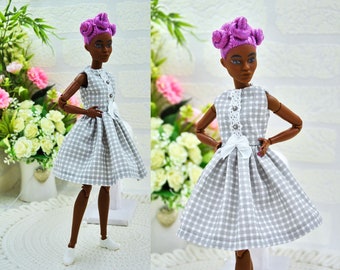May include: A doll wearing a gray and white gingham dress with a white bow and white lace trim. The doll has purple hair styled in buns and brown skin.