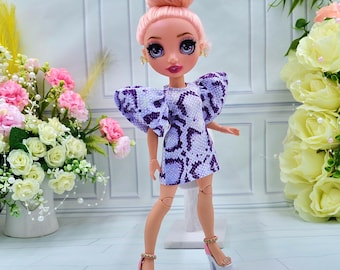 May include: A doll with pink hair styled in a bun, wearing a purple and white snake print dress with large puffed sleeves and white platform heels.