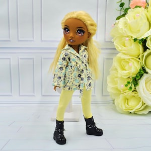 Puede incluir: Una muñeca con el pelo largo y rubio que lleva una chaqueta de estampado floral amarillo y azul, pantalones amarillos y botas negras.