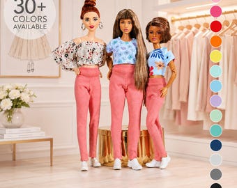 May include: Three dolls standing side by side, each wearing a cropped top and pink pants with white sneakers. The left doll has an off-the-shoulder floral top, the center doll has a blue patterned top, and the right doll has a blue floral top.