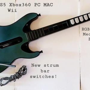 May include: A teal and black guitar-shaped game controller with the text "PS3 PS4 PS5 Xbox360 PC MAC Wii". Features include "RGB Lighted Mechanical Frets!" and "New strum bar switches!"