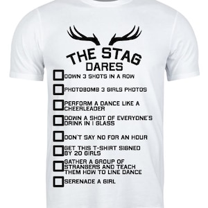 May include: White t-shirt with black text and graphics. The text reads "THE STAG DARES" above a list of dares, including "Down 3 shots in a row" and "Photobomb 3 girls photos". The shirt has a crew neck and short sleeves.