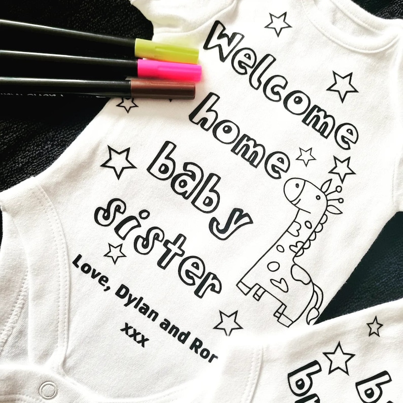 May include: White onesie with black text that reads "Welcome home baby sister" with a black and white giraffe illustration and stars. The text "Love, Dylan and Ror XXX" is also included.