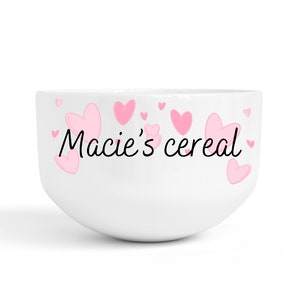May include: White ceramic bowl with pink hearts and the text "Macie's cereal" in black.
