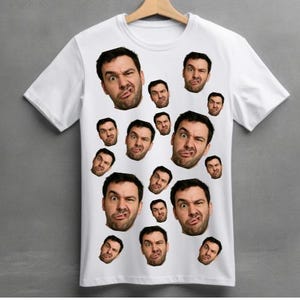 May include: White t-shirt featuring a pattern of various facial expressions. The faces are of a man with dark hair and a beard, making different funny faces. The shirt is hanging on a wooden hanger.