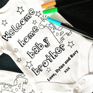 May include: White baby onesie with black outline of a giraffe and the text "Welcome home baby brother" and "Love, Dylan and Rory XXX".