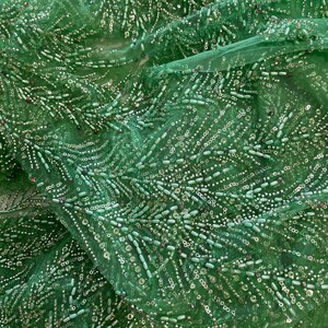 Peut inclure: Tissu vert perlé avec un dos en maille. Les perles sont disposées en un motif de lignes verticales.