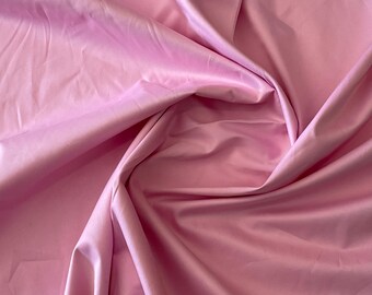 Puede incluir: Primer plano de una tela suave y rosa con una textura lisa. La tela está doblada y drapeada, creando un aspecto fluido y elegante.